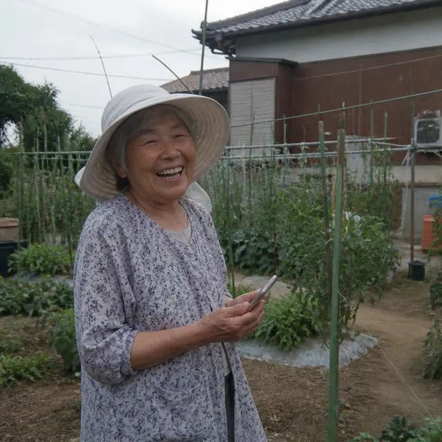 An older woman laughing in her garden while holding a phone